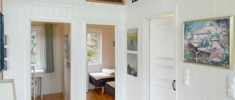 A room with a bed, a window, and a door. There are pictures on the wall and a painting above the door.