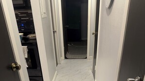 Un couloir doté d’un sol en marbre, un espace cuisine équipé d’appareils électroménagers et une porte donnant sur une autre pièce.