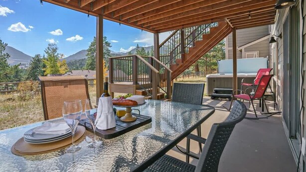 An outdoor dining area with a table set for two, a hot tub, and a staircase leading to an upper level. - Exceptional Views, hot tub -A Mountain Life! #3245 (Estes Park)