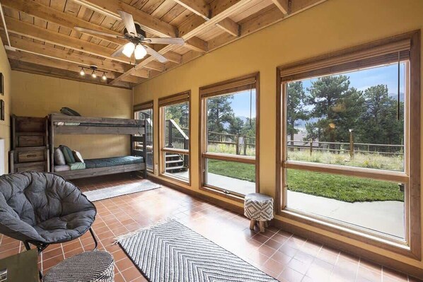 A rustic cabin interior with a bunk bed, a chair, large windows, and a ceiling fan. - Exceptional Views, hot tub -A Mountain Life! #3245 (Estes Park)