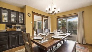 A dining room with a wooden table set for six, a chandelier, and a view of the outdoors through a sliding glass door. - Exceptional Views, hot tub -A Mountain Life! #3245 (Estes Park)