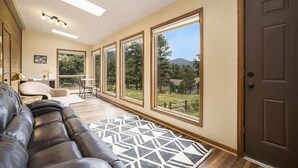 A spacious living room with a leather couch, a geometric rug, and large windows offering a view of the outdoors. - Exceptional Views, hot tub -A Mountain Life! #3245 (Estes Park)