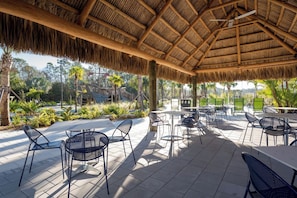 An outdoor patio area with thatched roof, tables, chairs, and a view of the surrounding landscape. - S-StoreyLake 9BR Sleeps 26 w/pool 5mil to Disney (Osceola County)