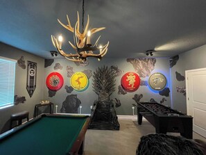 A pool table with a chandelier, a foosball table, and wall decor including animal prints and circular signs.