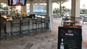An outdoor bar area with a television screen, bar stools, and a chalkboard menu.