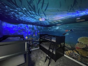 An underwater-themed room with bunk beds, a ceiling light, and a mural of marine life.