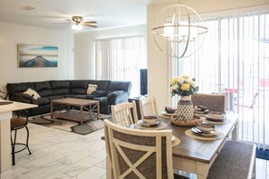 A living room with a sofa, coffee table, dining table with chairs, and a chandelier.