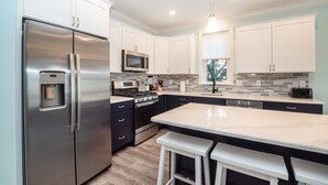 A modern kitchen with stainless steel appliances, white cabinetry, and a marble countertop. - Spacious Beach Block Home: 3 Beds/2 Baths, Front Porch w/ Furniture Included (Ocean City)