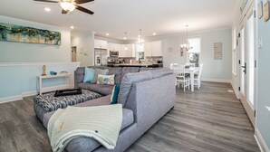 A modern living room with a grey sofa, ottoman, and a ceiling fan. - Spacious Beach Block Home: 3 Beds/2 Baths, Front Porch w/ Furniture Included (Ocean City)