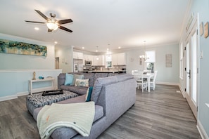 A modern living room with a grey sofa, ottoman, and a ceiling fan. - Spacious Beach Block Home: 3 Beds/2 Baths, Front Porch w/ Furniture Included (Ocean City)