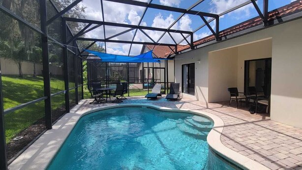 Ein Swimmingpool mit Glasverkleidung, umgeben von einer Terrasse mit Gartenmöbeln.