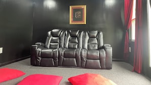Ein dunkler Raum mit einer Ledersofa, roten Kissen und einem gerahmten Bild an der Wand.
