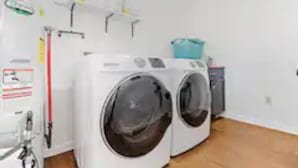 Ein Waschbereich mit zwei Frontlader-Waschmaschinen, einem Wäscheständer und einem kleinen Schrank.