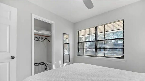 Ein Schlafzimmer mit einem großen Bett, einem Kleiderschrank mit Kleidung und einem Fenster mit Jalousien.