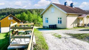 Une maison à deux étages avec une allée en gravier et une terrasse en bois équipée de chaises.