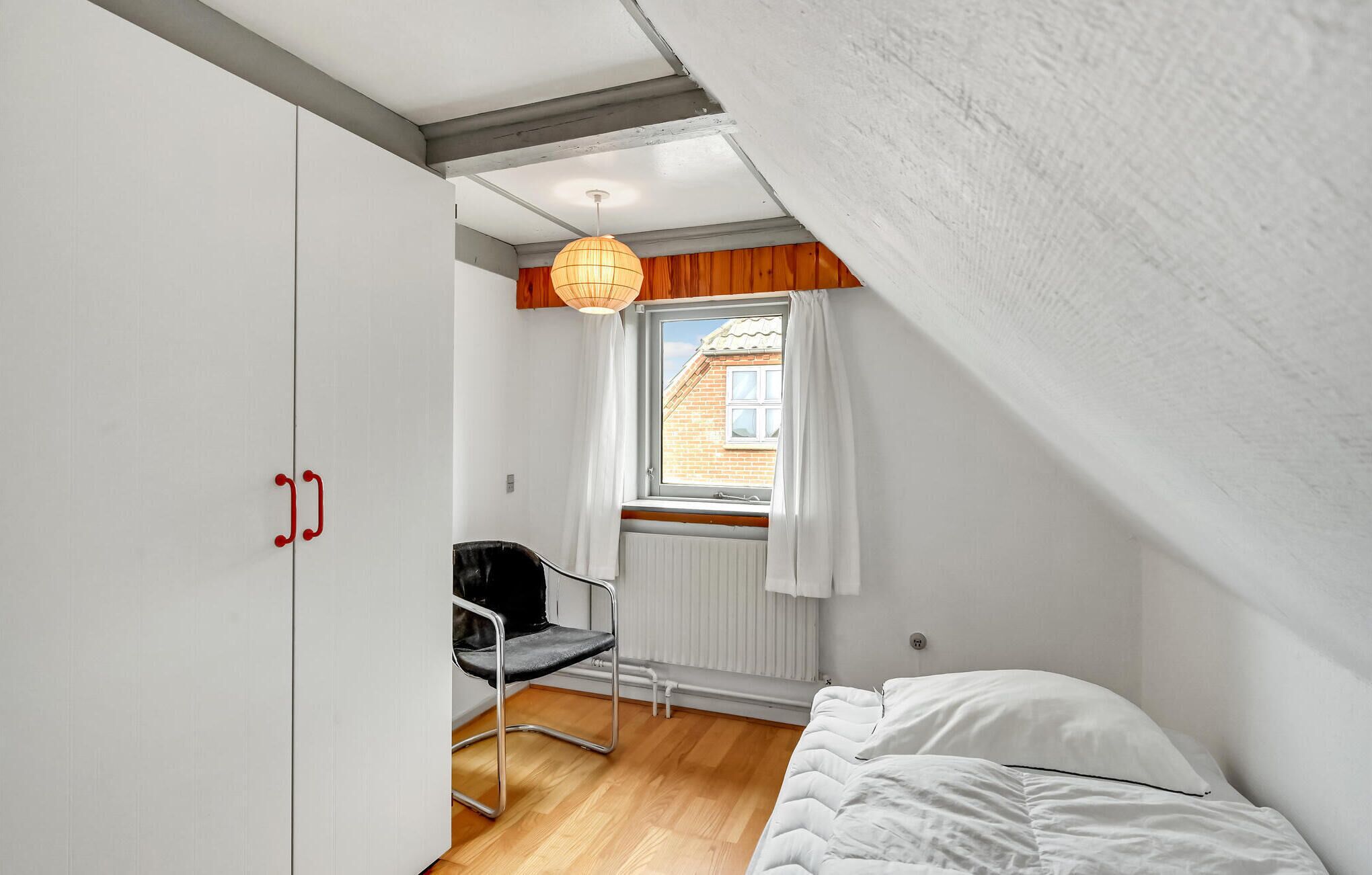 Ein Schlafzimmer mit Bett, einem Sessel, einem Fenster mit Vorhängen und einer Heizung.
