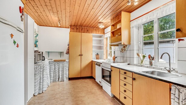 Eine moderne Küche mit Holzschränken, einer Edelstahl-Spüle und einem Fenster mit Tageslicht.
