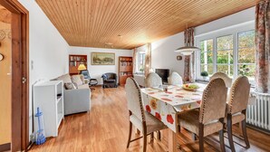 Ein Essbereich mit Holzboden, einem Tisch mit Blumenmuster-Tischdecke und Stühlen. An den Wänden befinden sich Bücherregale und ein Gemälde.