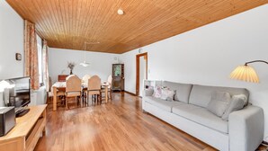 Ein geräumiges Wohnzimmer mit Holzbalkendecke, einem Esstisch mit Stühlen, einer Couch und einem Fernseher.