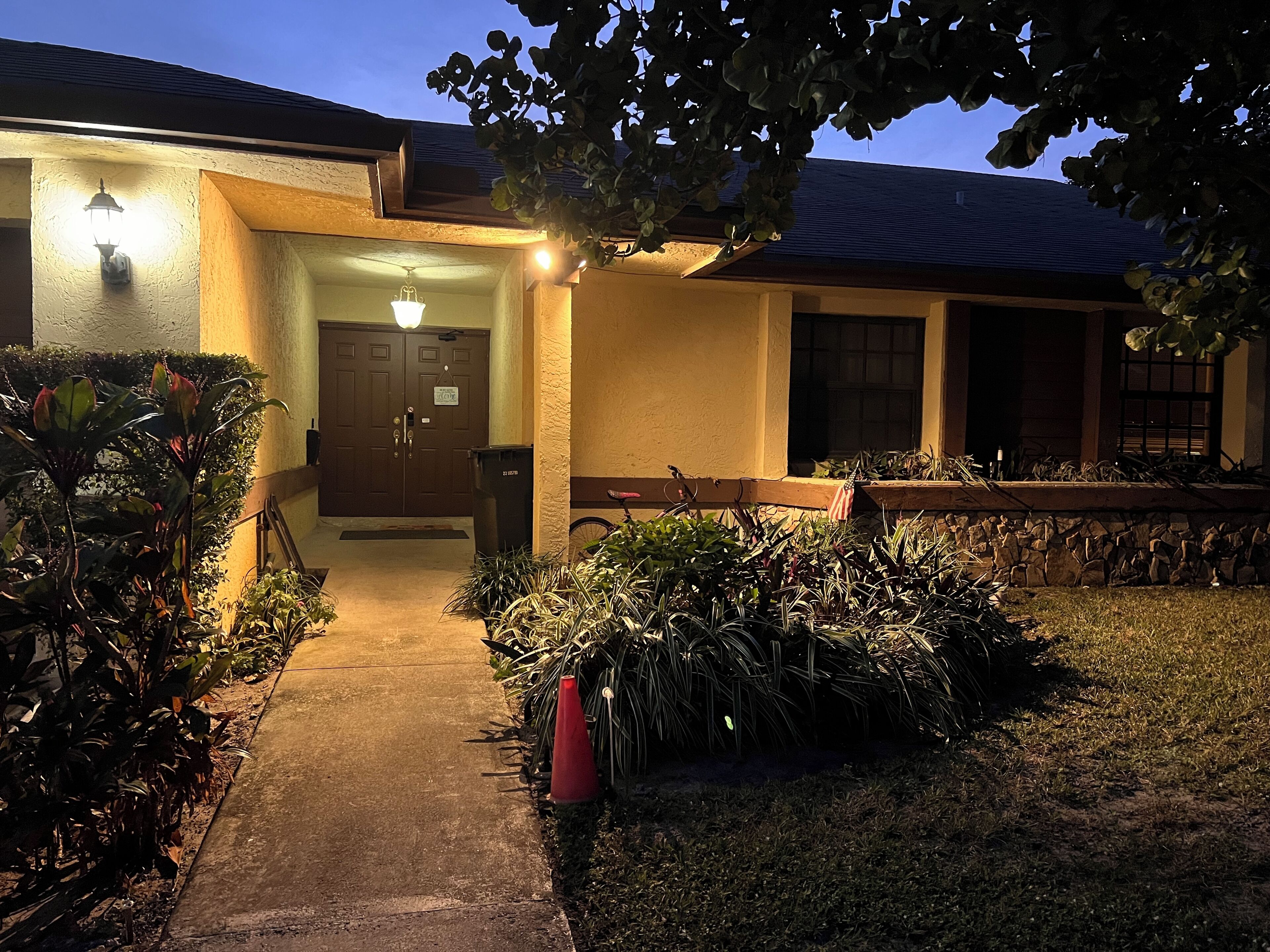A building with a well-lit entrance, a stone wall, and a pathway leading to the door.
