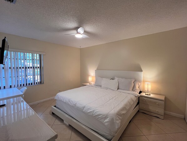 A bedroom with a bed, bedside tables, a desk, and a ceiling fan.