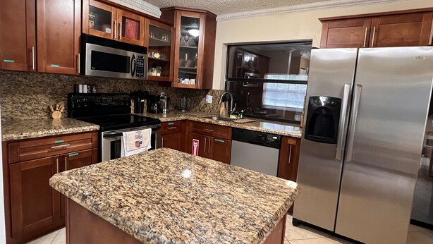 Cocina con encimeras de granito, electrodomésticos de acero inoxidable, armarios de madera y un microondas integrado.
