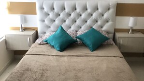 A bedroom with a tufted headboard, two teal pillows, a beige bedspread, and a wooden clock on the wall. - Amazing Condo with Pool - Magnífico Condo con Piscina (Yumbo)