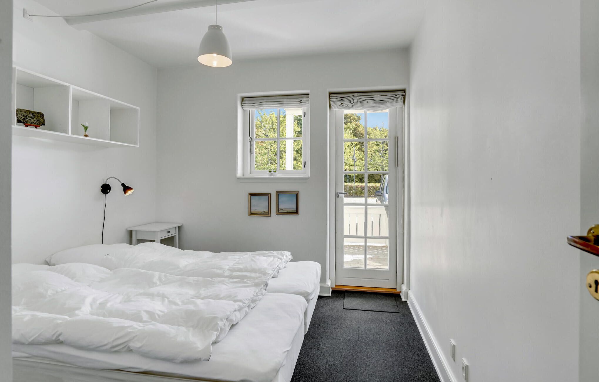 Quarto com cama, mesa de cabeceira, luminária e janela com vista para o exterior.