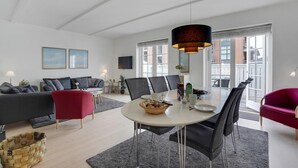 Un salon moderne avec un coin repas, comprenant une grande fenêtre, un téléviseur à écran plat et un fauteuil rouge.