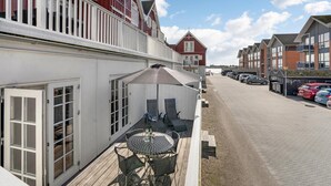 Une terrasse avec des sièges et une table, située à côté d’un bâtiment à la façade rouge et aux ornements blancs.