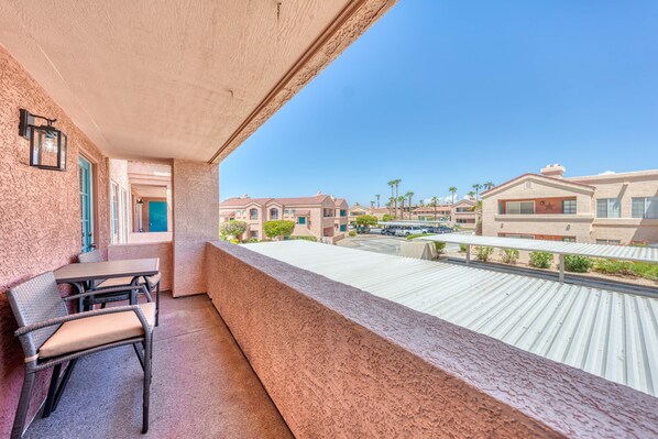 Un balcón con mesa y sillas, con vistas a una zona residencial con casas y un estacionamiento.