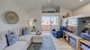 Una sala de estar moderna con sofá, mesa de centro y televisor. Hay un balcón con vista a edificios.