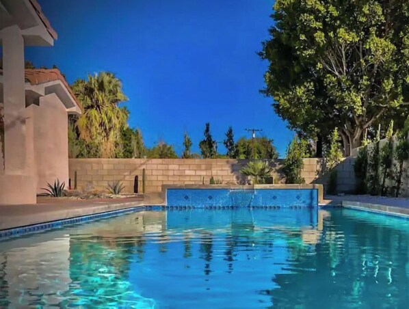 Relax by the tranquil pool surrounded by lush greenery and a clear blue tile border.