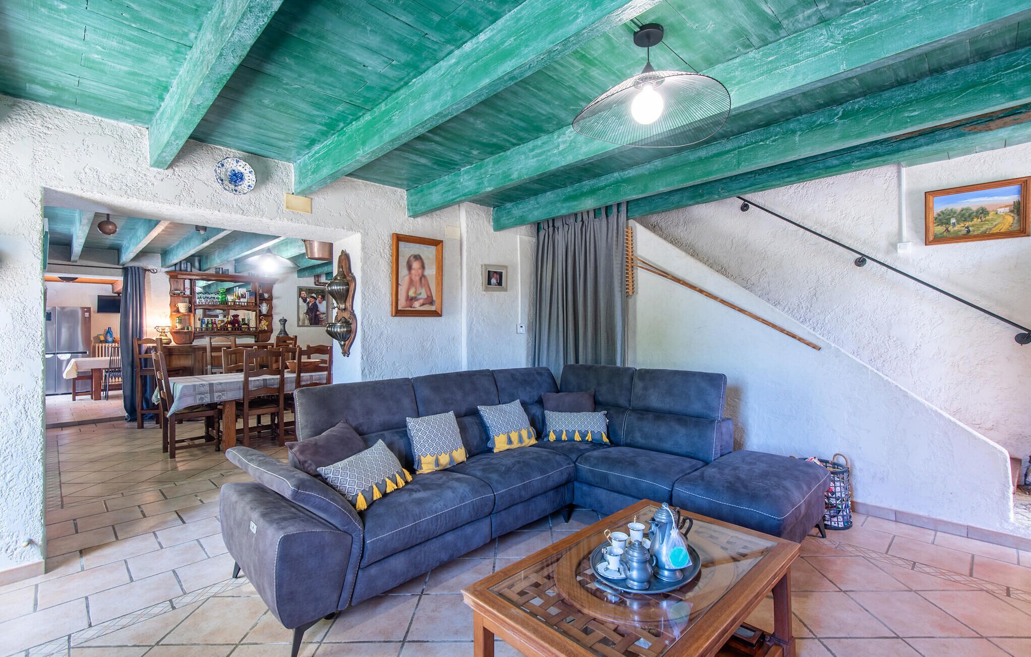 Een woonkamer met een hoekbank, een bijzettafeltje met theeservies en een trap met een groen plafond.