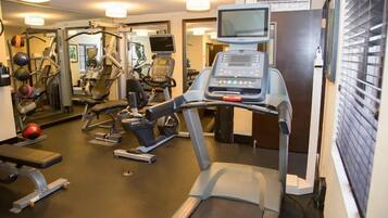 A gym with treadmills, exercise balls, and a television screen.