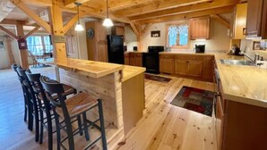 A spacious kitchen with wooden beams, a central island with bar stools, and a large refrigerator. - Lakeside Haven - Ice fishing, Snowmobiling, Skiing (Denmark)