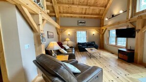 A spacious living room with a high wooden ceiling, a leather sofa, a coffee table, and a television mounted on the wall. - Lakeside Haven - Ice fishing, Snowmobiling, Skiing (Denmark)