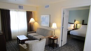 A hotel room with a sofa, a small table, a lamp, a bed, and a carpeted floor.