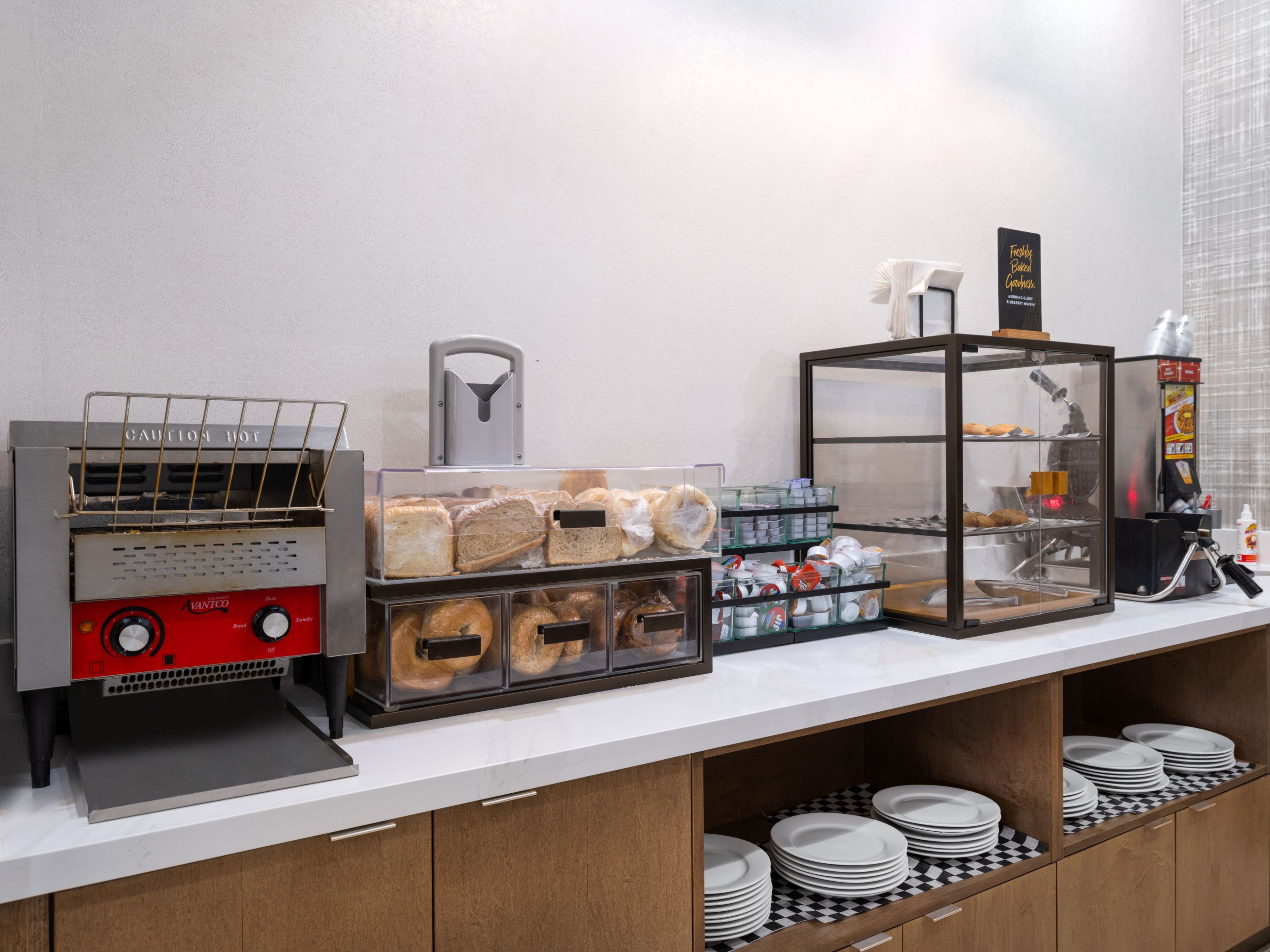 Un espace buffet pour le petit-déjeuner avec un présentoir à pains, une machine à café et un espace réfrigéré.