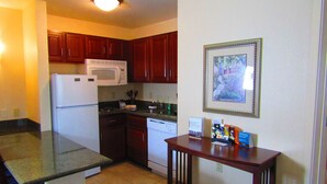 A kitchen with wooden cabinets, a white refrigerator, a microwave, a dishwasher, and a small table with a framed picture on the wall. - Suite Near Rochester University | Gym Access (Rochester)