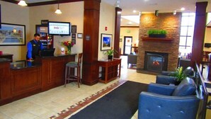 A hotel lobby with a reception desk, seating area, fireplace, and a large window. - Suite Near Rochester University | Gym Access (Rochester)