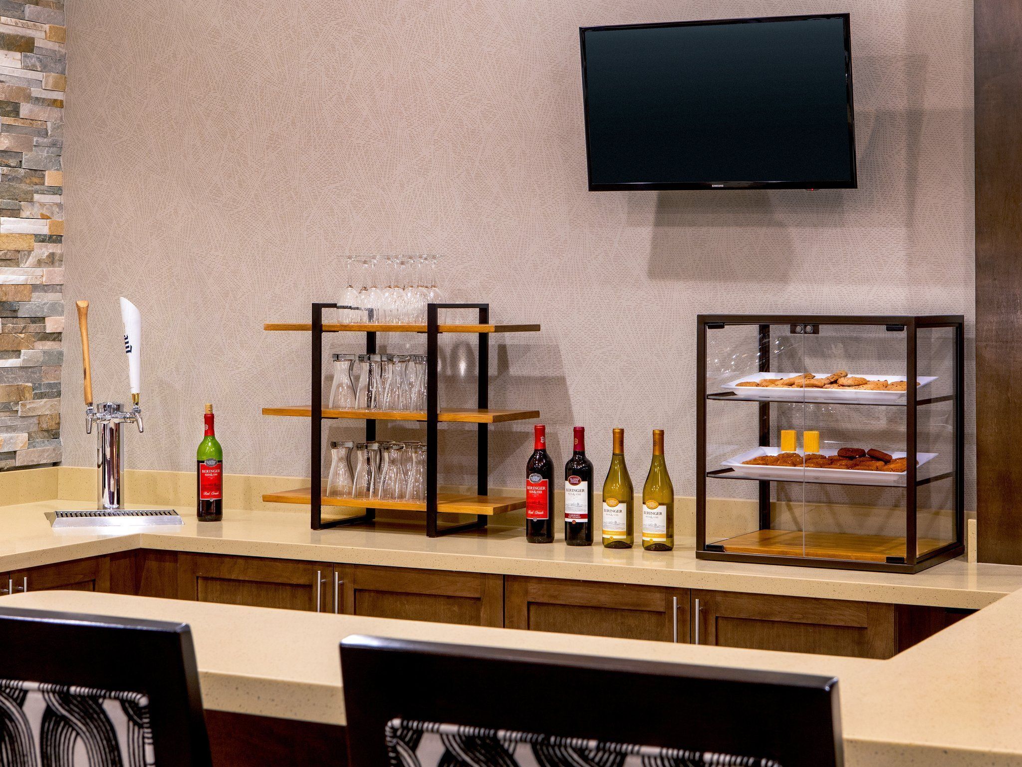 Un espace bar avec un robinet, des bouteilles de vin, des verres et un présentoir contenant des pâtisseries.