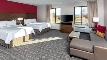 A hotel room with two beds, a sofa, a TV, and a window with a view of the outdoors.