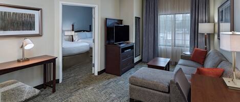 A hotel room with a bed, a TV, a desk, a sofa, and a carpeted floor.