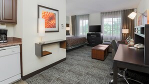 Quarto de hotel com cama, escrivaninha, cadeira, televisão e cafeteira.