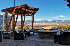 Une terrasse extérieure avec des sièges en pierre, un foyer et une pergola offrant une vue sur un paysage montagneux.