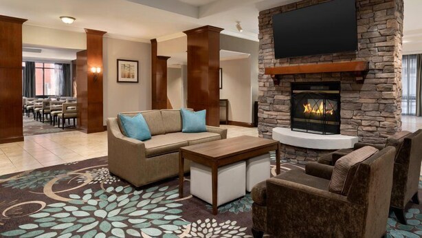 A hotel lobby with a stone fireplace, a flat-screen TV, and a seating area with a sofa and armchairs. - Comfy Studio Suite | Free Breakfast + Outdoor Pool (San Antonio)