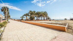 Une promenade dallée bordée de palmiers, un espace de jeux et, au loin, une plage.