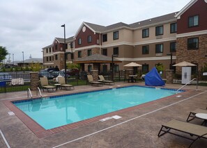 A swimming pool with lounge chairs and umbrellas, surrounded by a building with stone and wood exterior.