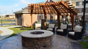 Een terras met een vuurkuil van steen, buitenmeubels en een houten pergola.